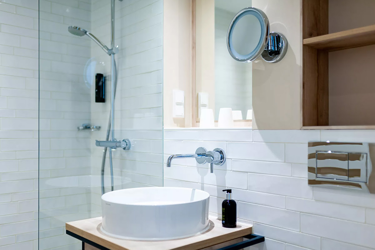 Elegantes Badezimmer mit großer Glasdusche, rundem Waschbecken und Holzdetails im Zimmer Buhne des Wyn. Strandhotels.