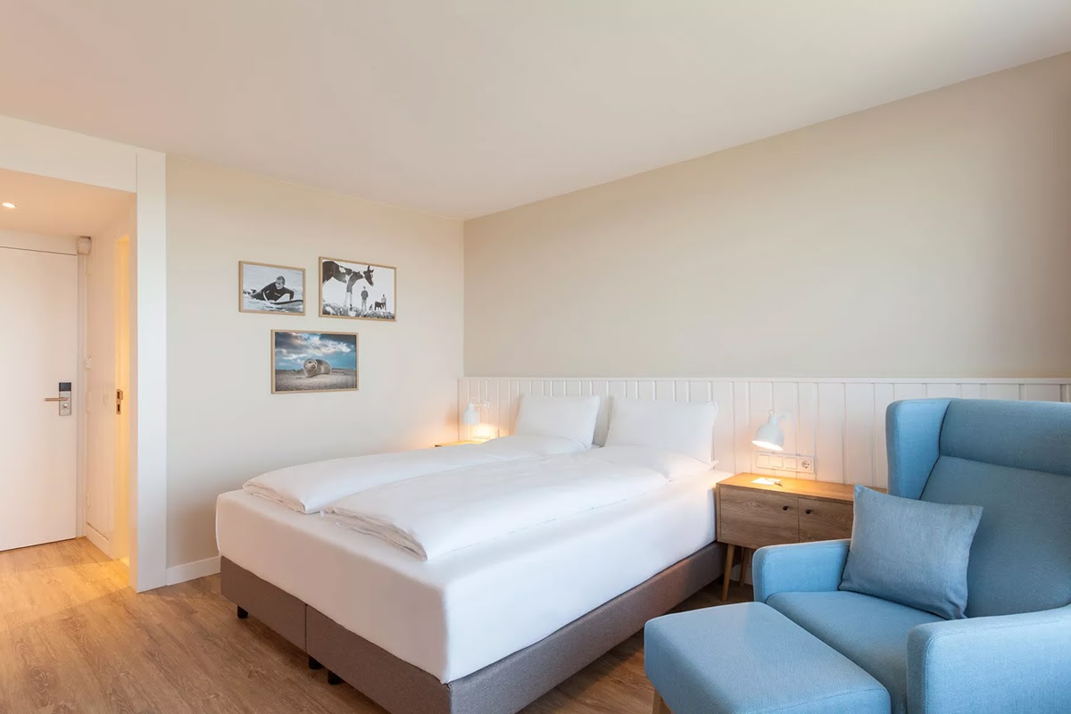 Inviting hotel room Meerzeit with comfortable bed, blue armchair and soft lighting in the Wyn. Strandhotel.