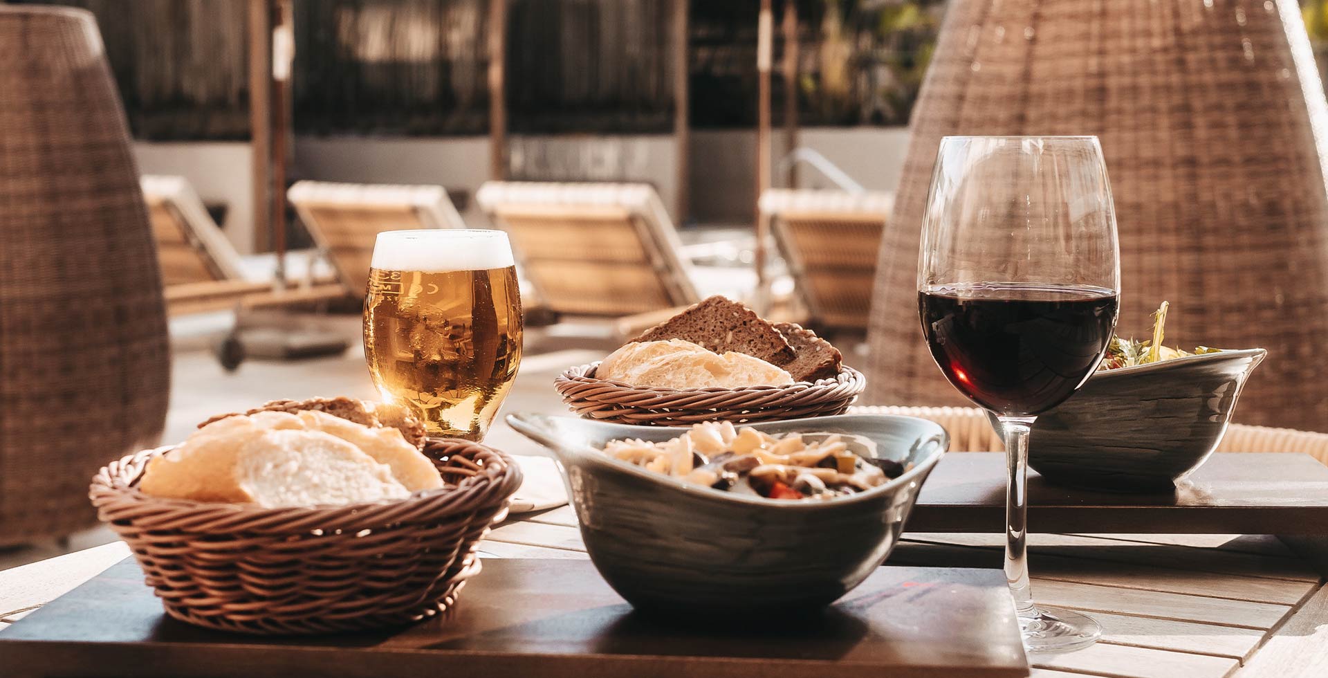 Ein reich gedeckter Tisch mit Pasta, Salat und Brot, dazu Bier und Wein. Im Hintergund Wellness-Liegen im Außenbereich des Hotels.