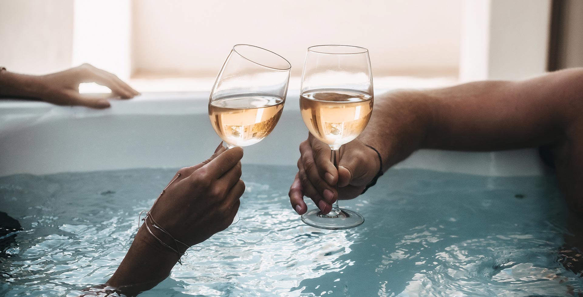 Zwei Personen stoßen im Whirlpool mit Wein an.