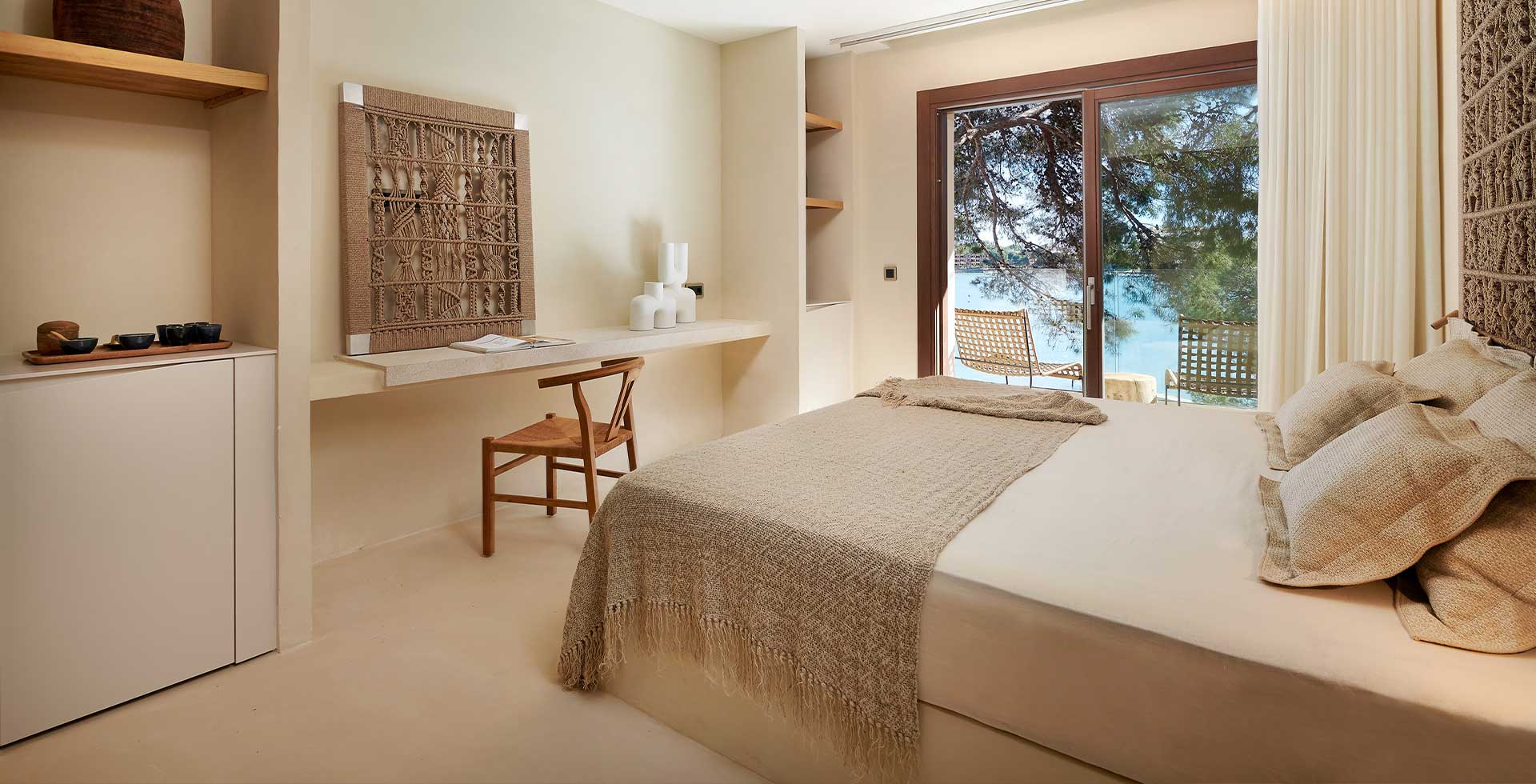 Hell eingerichtetes Doppelzimmer mit Naturmaterialien und Flechtelementen, Balkon mit Blick auf die Bucht.