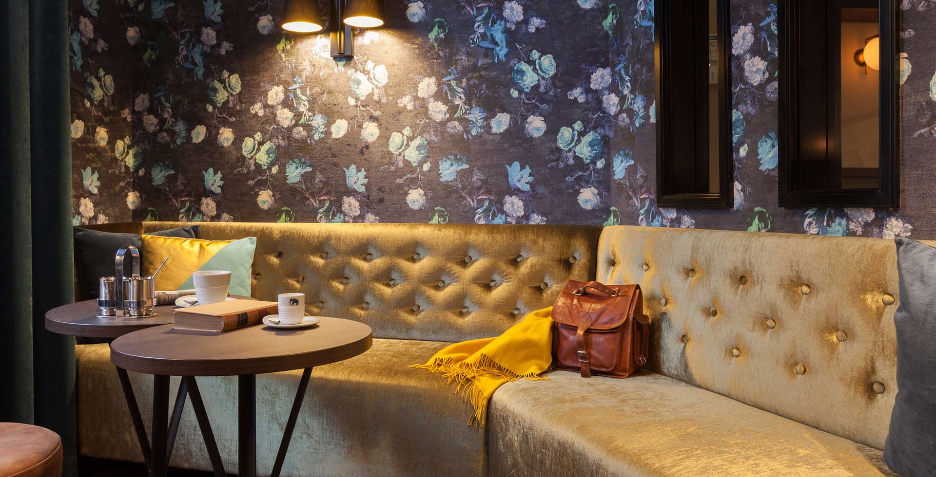 Klassisch anmutende, goldgelbe Samt-Sitzbank mit Knopfheftung vor blauer Rosentapete in der Weinkost Bar des Hotels.