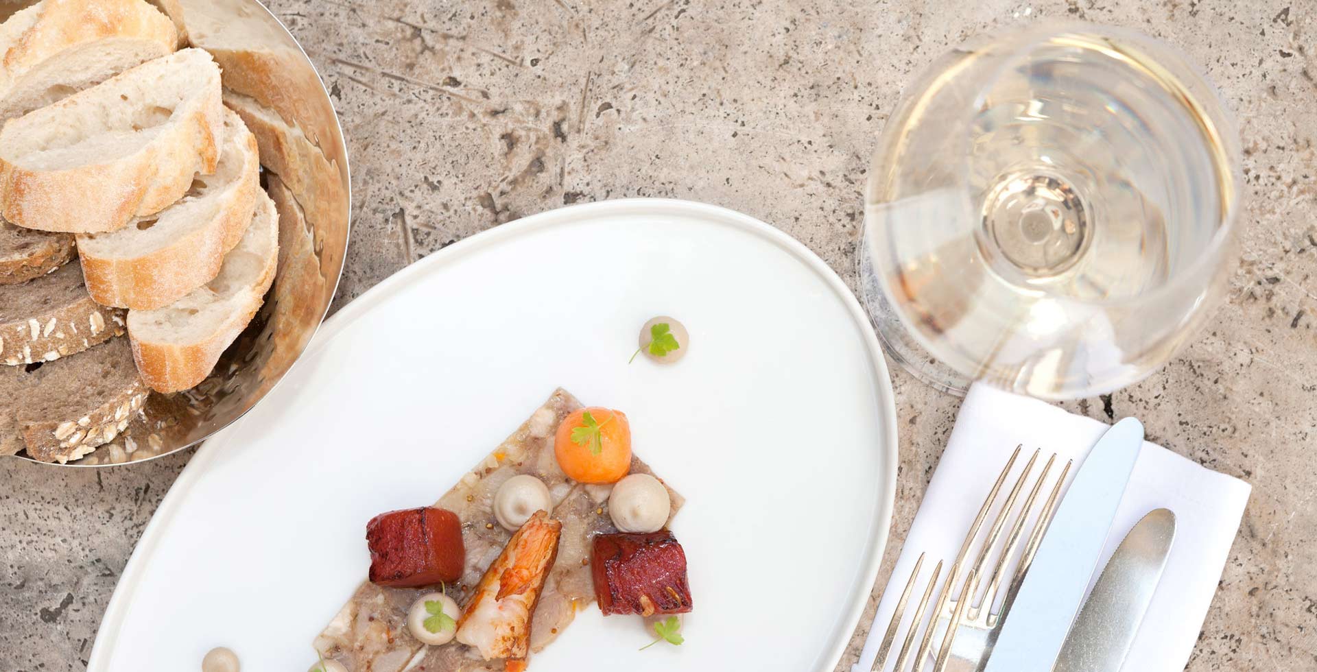 Eine fein abgestimmte Mahlzeit aus Fisch, Meeresfrüchten und Gemüse mit Brotbeilage und Weißwein, kunstvoll angerichtet auf einem Steintisch.