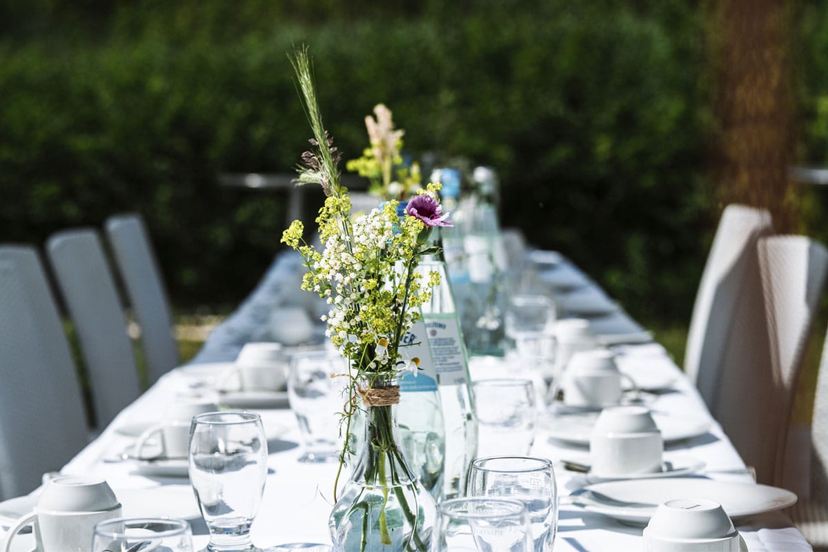 Lange gedeckte Tafel im Freien mit Blumenarrangement und gedecktem Geschirr für eine Hochzeit im Hotel Seezeichen.
